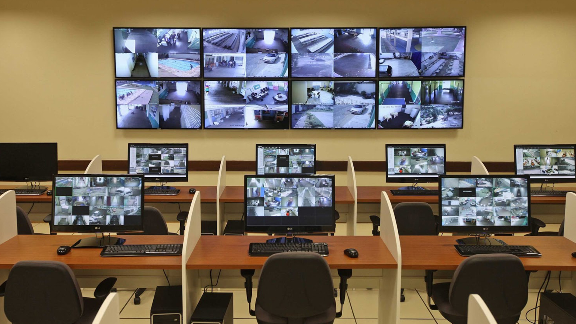 Imagem de uma sala de monitoramento com vários computadores em mesas dispostas em fileiras.